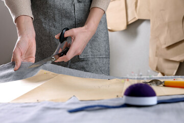 Tailor cutting fabric with scissors at table in atelier, closeup