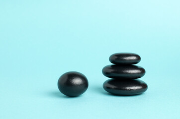 A stack of black zen balance stones on a blue background. The concept of a SPA center. A stage for promotion, sale, presentation or cosmetics. Copy space