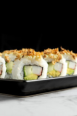 Close up of Sushi rolls with crab and avocado with crispy onion and mayonnaise topping on a marble table with black background. High quality photo