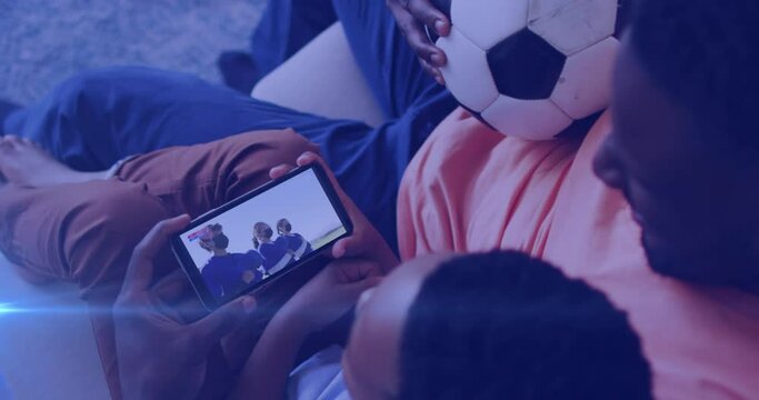 Animation of glowing lights over african american man with son watching football on smartphone