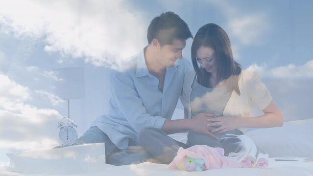 Animation of clouds over happy caucasian man embracing pregnant wife