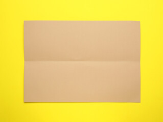 Sheet of brown paper on yellow background, top view