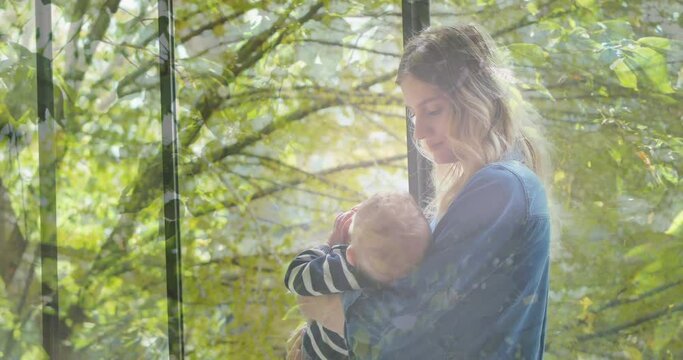 Animation of trees over happy caucasian mother holding her baby