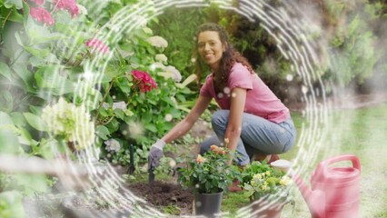 Animation of white circles spinning and glowing spots over happy biracial woman gardening
