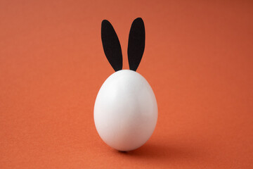 White easter egg with bunny ears on orange background.
