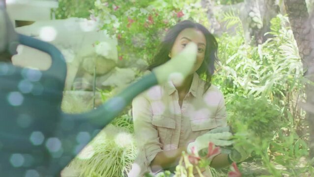 Animation of glowing spots over happy biracial couple with watering can gardening - Powered by Adobe