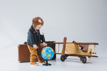 A boy in a leather jacket and a pilot's hat, a wooden plane, a globe, brown suitcases. Children's...