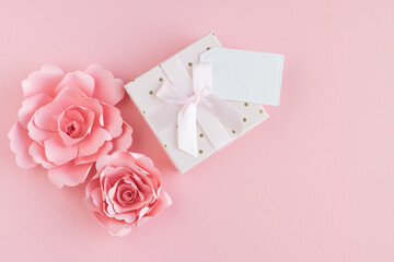 Paper roses with gift box and blank card on pink background. Copy space.