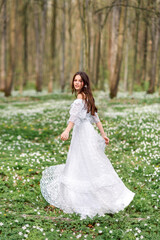 Obraz na płótnie Canvas girl in a white long dress is spinning in a clearing with flowers. A young woman with long hair in a spring forest.
