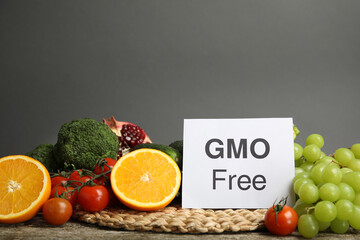 Tasty fresh GMO free products and paper card on wooden table against grey background