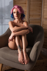 seductive young woman with tattoo sitting on armchair.