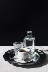 Black coffee with a glass and pitcher of water on an elegant silver tray with a dark background