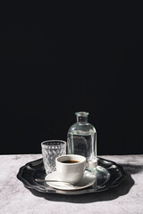 Black coffee with a glass and pitcher of water on an elegant silver tray with a dark background