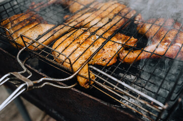 Chicken thighs are fried on the grill in a barbecue on a fire with smoke in nature.