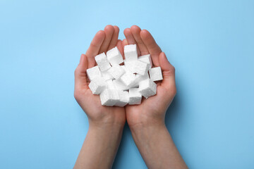 Woman with handful of styrofoam cubes on light blue background, top view
