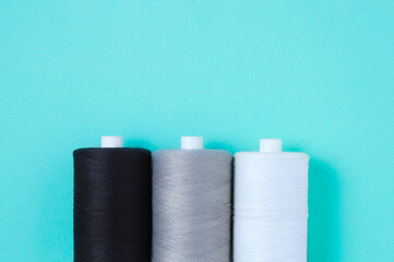 Three spools of sewing thread lie in  row. Place for text. Turquoise background.
