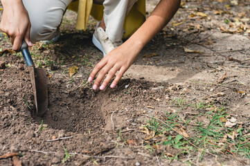 woman digging a hole in the ground with a hand shovel to transplant a plant