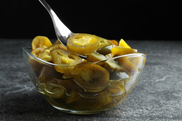 Taking slice of pickled green jalapeno with fork from bowl on grey table