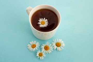 Obraz na płótnie Canvas Chamomile tea. On a blue background, a white cup with tea and daisies