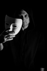 Black and white portrait of a young hooded man taking off his mask, concept for being true and authentic