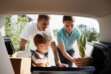 Portrait of smiling family loading boxes in car trunk while moving into new house in sunlight