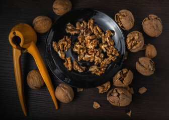 Nuts. Walnut kernels and whole walnuts. Walnuts organic in a black bowl  on a dark wood background. Top view. Walnut healthy food. Nuts. Walnut kernels and whole walnuts. 