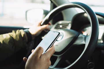 Handling your phone while driving. Close-up of a hand holding a phone and steering wheel of a car while driving.