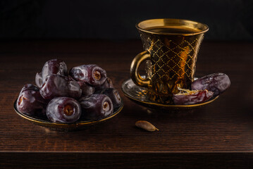 Still life coffee in a  golden oriental cup served with sweet Mazafati 
 dates on wooden dark background