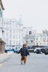 Stylish boy 3 years old in a leather jacket and brown trousers walks on the street. Modern child. Children's fashion. Happy child