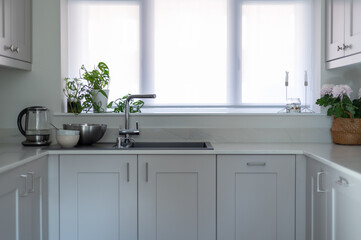 Modern new kitchen with light grey furniture and quartz worktop, light interior trendy units. Granite sink under big window