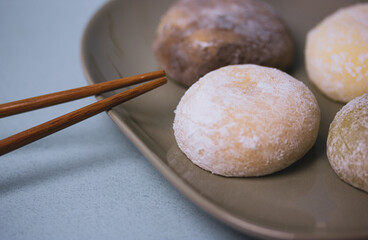 Traditional Japanese dessert mochi in rice dough or daifuku. Mochi ice cream balls and gray plate, food chopsticks on blue grey background. Table setting. Selective focus. Yomogimochi rice cakes.