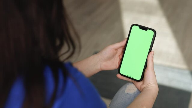 Closeup of woman holds mobile phone smartphone and swipes photos or pictures left indoors of cozy home. Chroma key mock-up on smartphone in hand. Use green screen for copy space