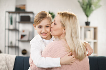 Close up smiling happy caucasian little boy embracing mum or babysitter, kissing on the cheek, holding, hugging each other, young woman hug small adopted daughter.