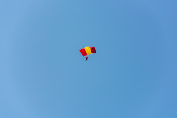 A red-yellow parachutist is planning against the blue sky.