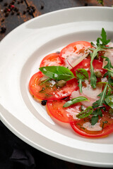 Light Salad with thinly sliced tomatoes, arugula, parmesan, capers and balsamic sauce. Vegetarian tomato salad on wooden table
