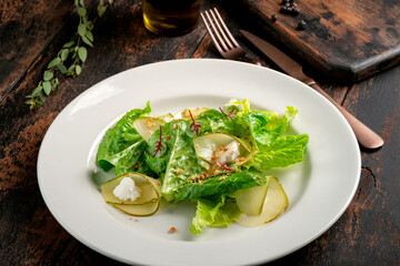 Fresh green salad with pear, rocket leaves, cheese and nuts on a white plate. Vegetarian salad on a wooden background, close up
