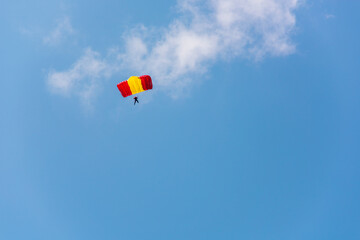 A red-yellow parachutist is planning against the blue sky.