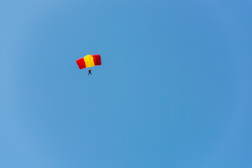 A red-yellow parachutist is planning against the blue sky.