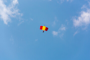 A red-yellow parachutist is planning against the blue sky.