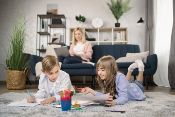 Family, leisure and people concept - happy mother with tablet pc computer laptop sitting on sofa and looking at daughter and son drawing at home