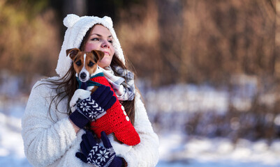 Young woman in winter jacket holding her Jack Russell terrier on hands - blurred trees background