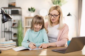 Fototapeta premium Caucasian tutor engaged with schoolgirl help complete tasks sitting at table at home. Concept of education kid development, european child homeschooling writing homework with stepmother concept