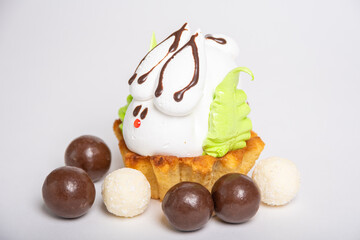 Side view of a homemade protein cake in the shape of an Easter bunny nestled on a biscuit cookie among round chocolates. Sweet Easter tradition. spring holiday. Easter treat for kids