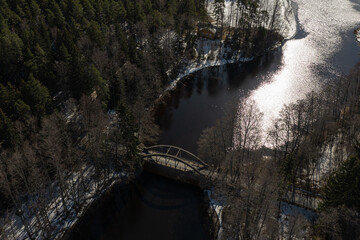 Bridge across the river. Landscape over a forest and a lake covered with ice and snow. Drone photo. Scandinavia. Finland.