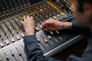 Close up of male hands operating buttons and toggles at digital audio workstation in recording...