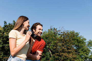Low angle view of cheerful woman holding binoculars near boyfriend outdoors.