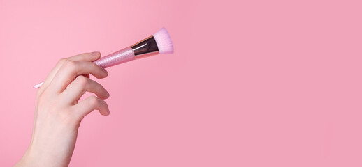 Hand holding makeup brush on pink background. Ad banner with copy space.