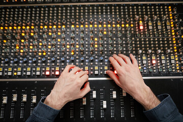 Top view background of male hands operating buttons and toggles at audio workstation in...