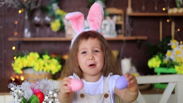 easter, a little girl in the ears of a hare plays with Easter eggs closing her eyes, smiles and prepares for the holiday at home in the kitchen