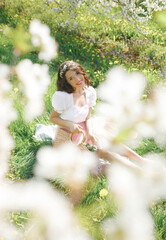 Natural woman with wreath on head and wicker handbag in summer garden enjoying blooming nature